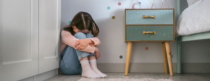 Sad little girl sitting on the floor of her bedroom