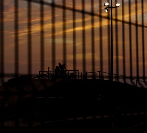 Silhouette family at skateboard park seen through fence against sky during sunset
