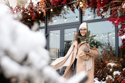 A cute girl with a scarf walks near the magenta shop window with a package of christmas nobilis