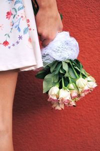 Midsection of woman holding bouquet against red wall