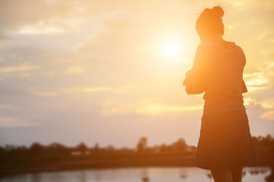 Side view of silhouette woman standing against sky during sunset