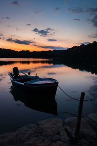 Boat moored in lake against sky during sunset