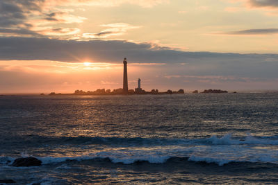 Lighthouse by sea against sky during sunset