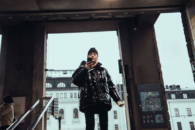 Low angle view of young woman using mobile phone while standing against doorway in subway