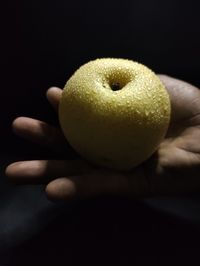 Close-up of hand holding pear against black background
