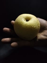 Close-up of hand holding apple against black background