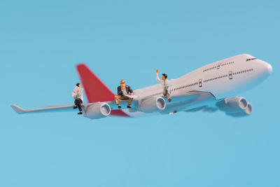 Close-up of male figurines sitting on model airplane against blue background