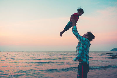 Boy standing on beach against sky during sunset