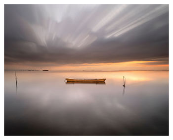 Boat moored in lake against dramatic sky during sunset