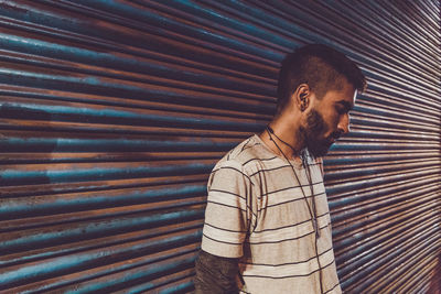 Young man looking down while standing against closed shutter