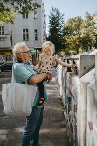 Grandfather carrying daughter trashing garbage while standing at street