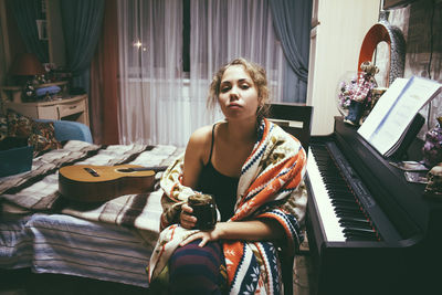 Portrait of woman with drink sitting by instruments on bed at home