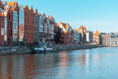 Buildings by river against clear sky