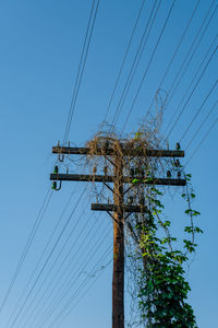 Low angle view of electricity pylon against clear blue sky