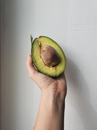 Close-up of hand holding apple against wall