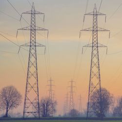 Low angle view of electricity pylon against sky during sunset