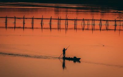 Silhouette man fishing in sea against sky during sunset