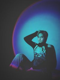 Portrait of young woman sitting against black background