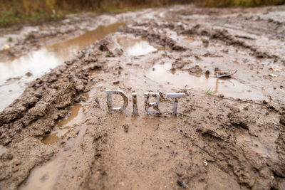 Word dirt composed of silver metal letters on wet clay surface with selective focus, background blur 