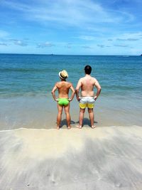 Rear view of shirtless friends standing at beach against sky