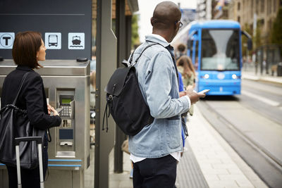 Commuters standing on sidewalk while waiting for tram in city