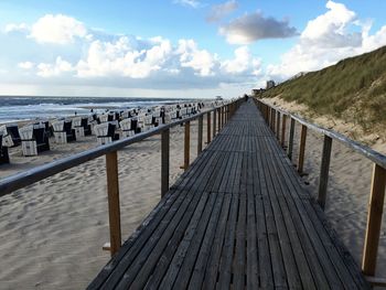 Wooden walkway leading towards sea against sky