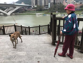 Full length of woman with umbrella by dog at observation point in city