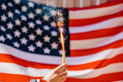 Cropped hand holding lit firework against american flag