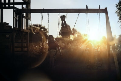 People on swing in playground against sky