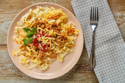 Pasta bolognese in tomato garnished with herbs and cheese in a plate on a wooden table