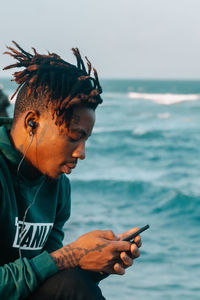 Young man holding camera by sea against sky