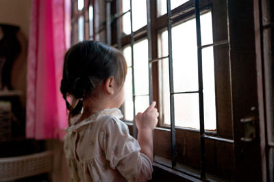 Side view of girl looking through window at home
