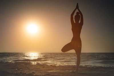 Low section of woman doing yoga at beach against sky during sunset