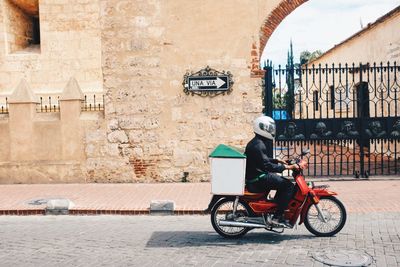 Side view of man riding motor scooter on street