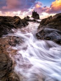 Scenic view of waterfall against sky during sunset