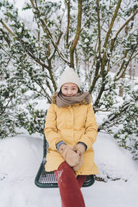Portrait of young woman sitting on snow covered field