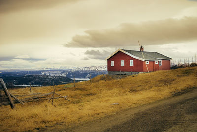 House on field by buildings against sky