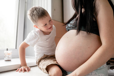 Smiling boy looking at pregnant mother stomach in house