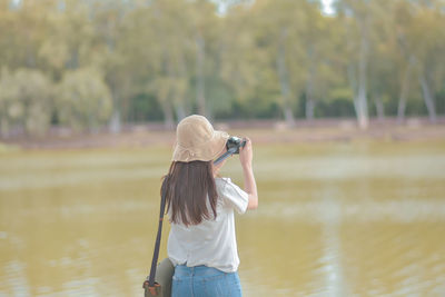 Rear view of woman photographing against trees