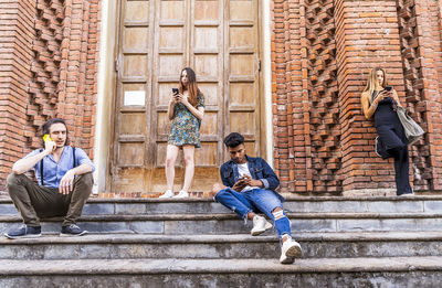 Full length of friends sitting on staircase against building