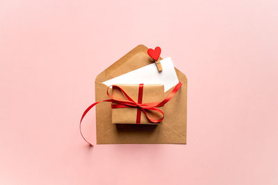 Creative valentine day composition with paper envelope, red heart and gift box on pink background.