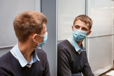 A young man in a protective mask looks in the mirror