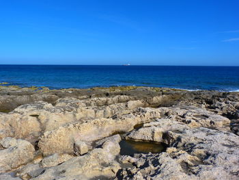 Scenic view of rocks on beach against clear blue sky