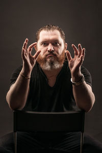 Portrait of man sitting against black background