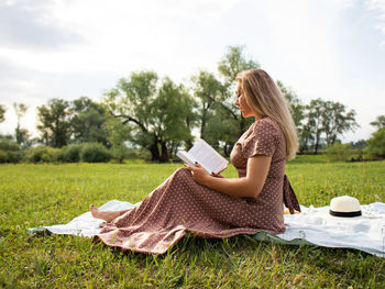 Young woman in a summer dress makes a selfie while sitting on a picnic in nature, 