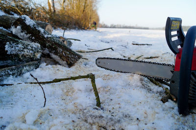 Chainsaw by chopped firewood on snow covered field