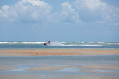 Distant view of people riding jet boat on sea against cloudy sky