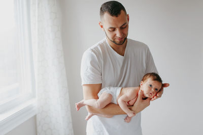Father carrying daughter while standing by window