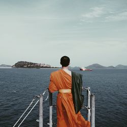 Rear view of monk looking at sea against sky