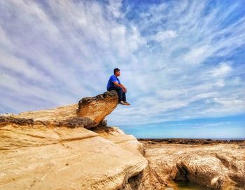 Low angle view of man sitting on rock formation at beach